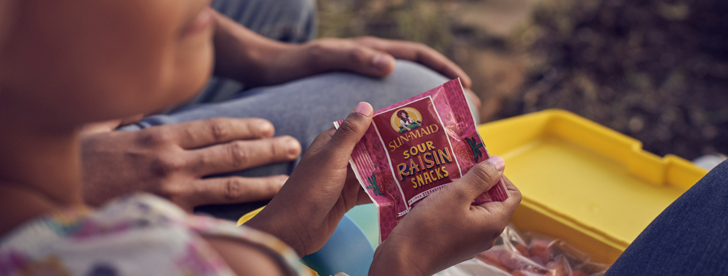 Girl with a pouch of Sun·Maid Sour Raisin Snacks in hand