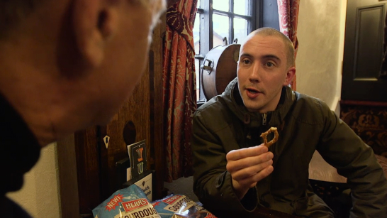 Man talking to Ed Herr while holding a pretzel in a pub