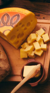 Part of a Jarlsberg cheese wheel and cheese cubes on a cutting board