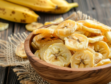 A wooden bowl filled with crispy banana chips on a rustic table, with fresh bananas in the background.