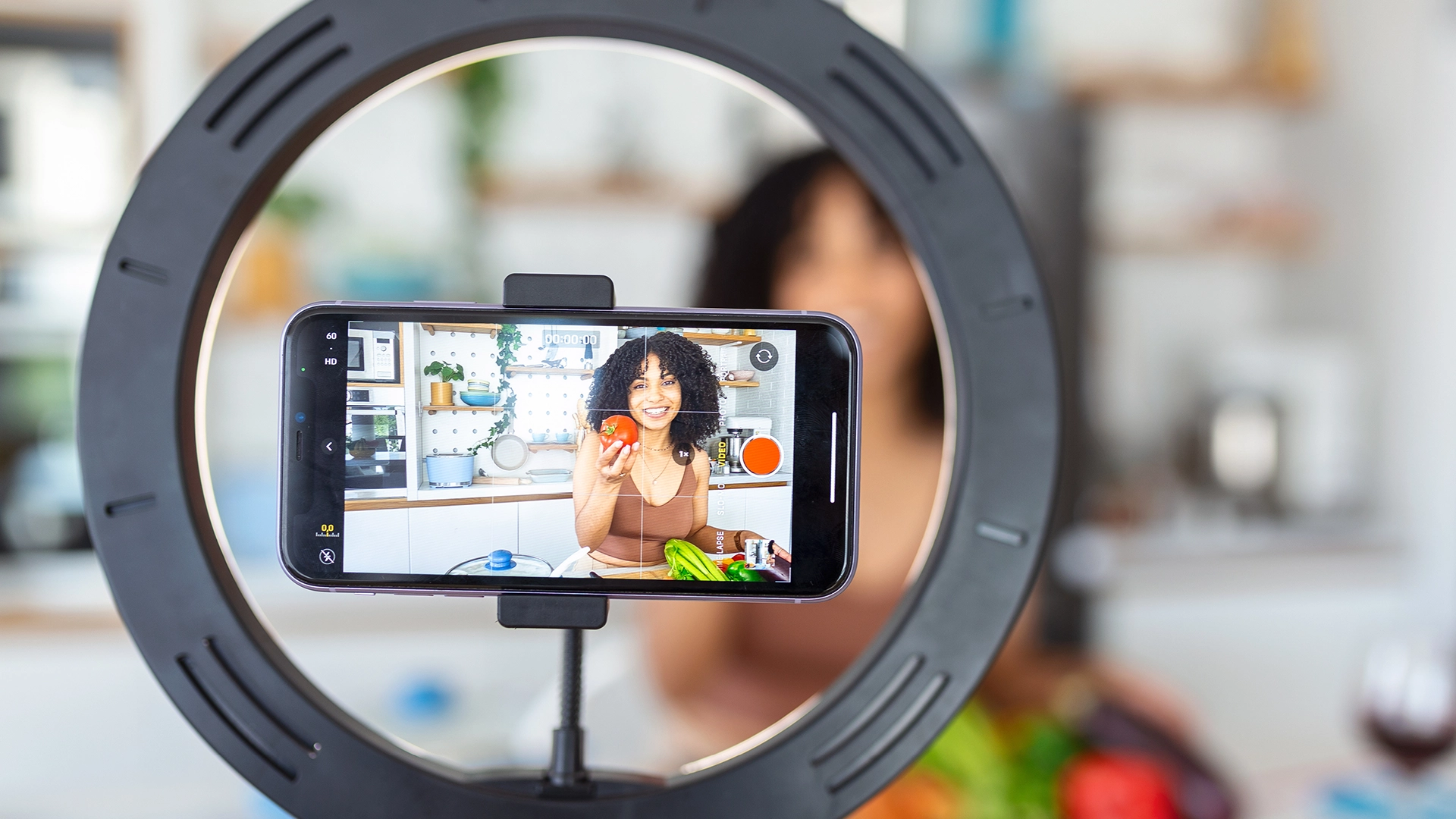 Woman holding fruit in a kitchen, recording a video on her phone with a ring light, showing how personable nano-influencers are.